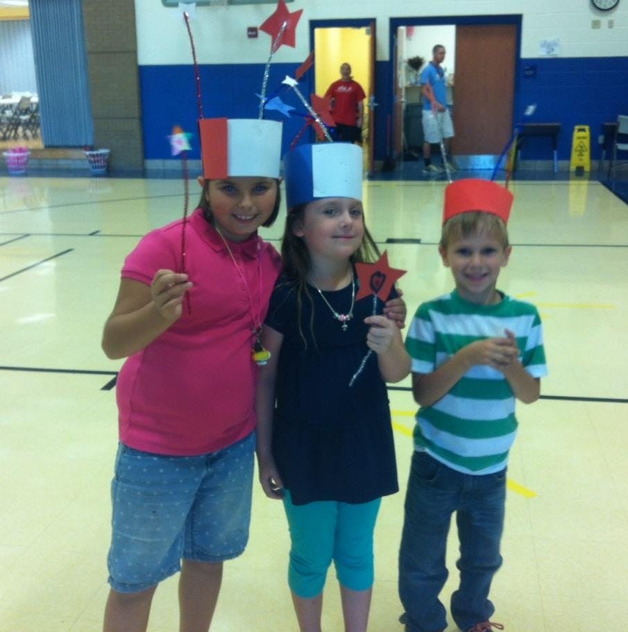 Three children wearing paper hats and holding star wands