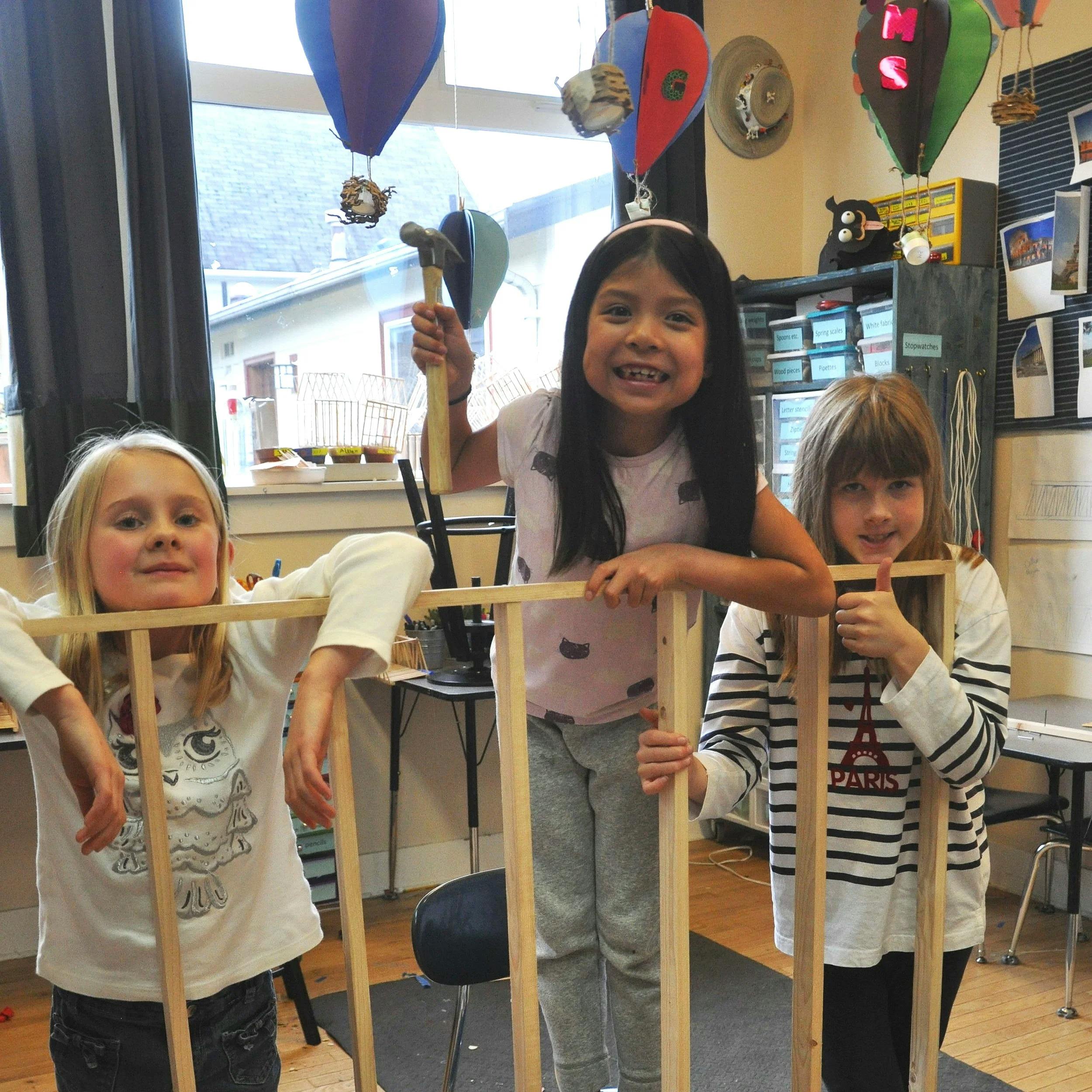 Three children constructing a wooden frame in a classroom