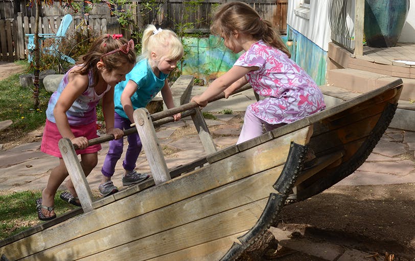 Three children playing on a wooden boat structure