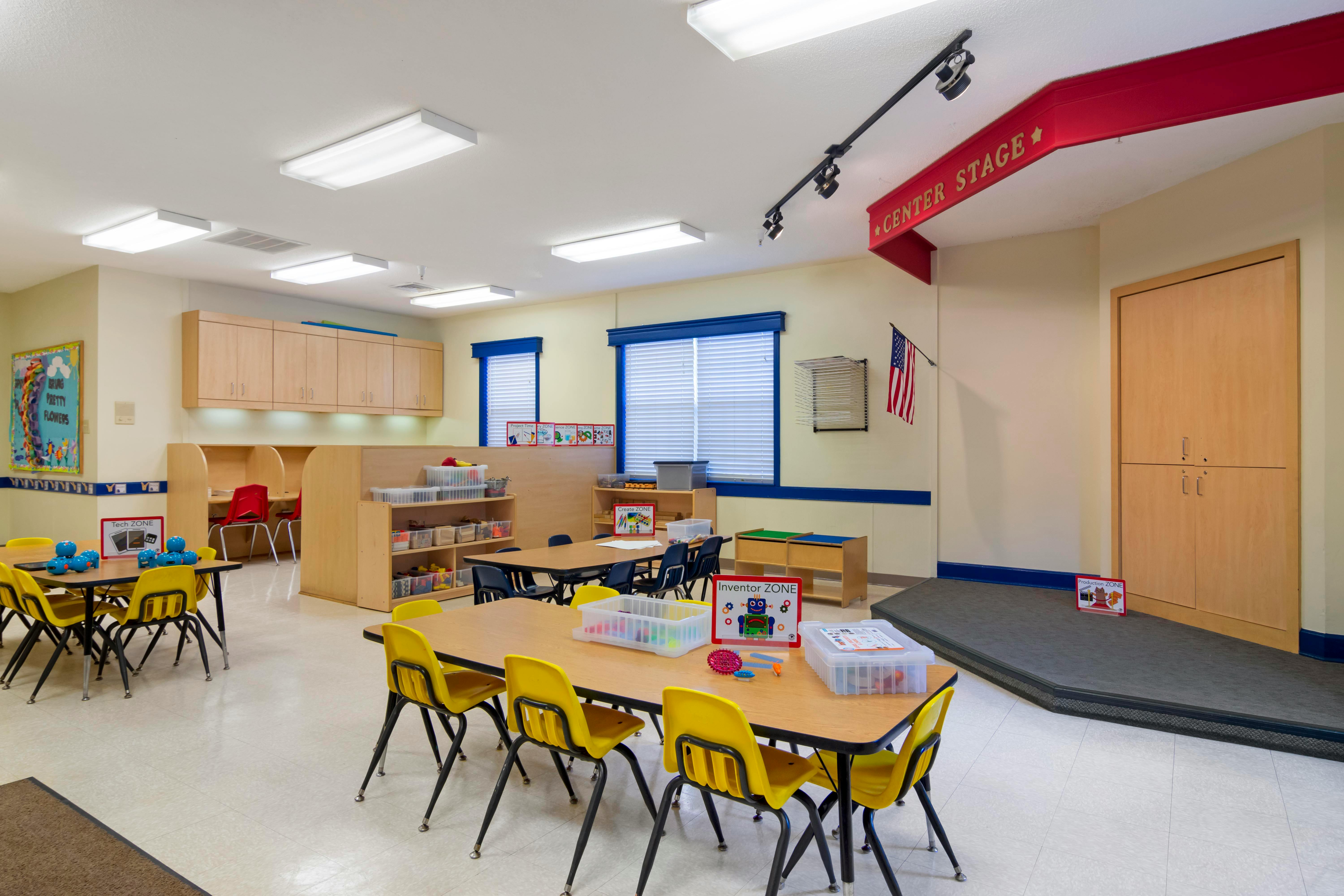 Classroom with small tables and chairs, shelves, windows, and an American flag