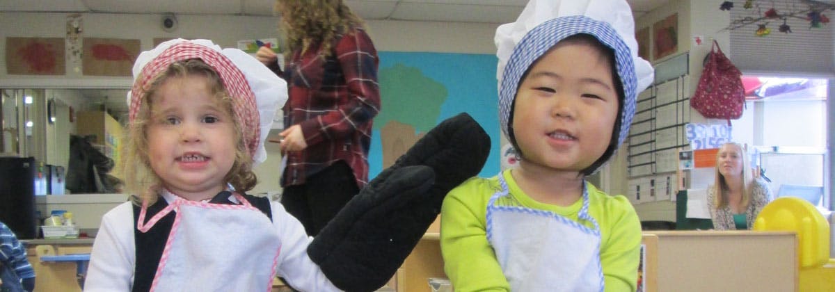 Two children wearing chef hats and aprons