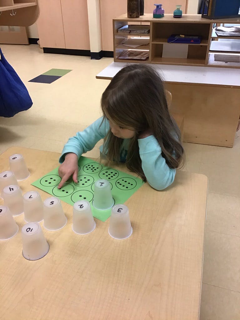 Child pointing at a green sheet with circles and dots, surrounded by numbered cups