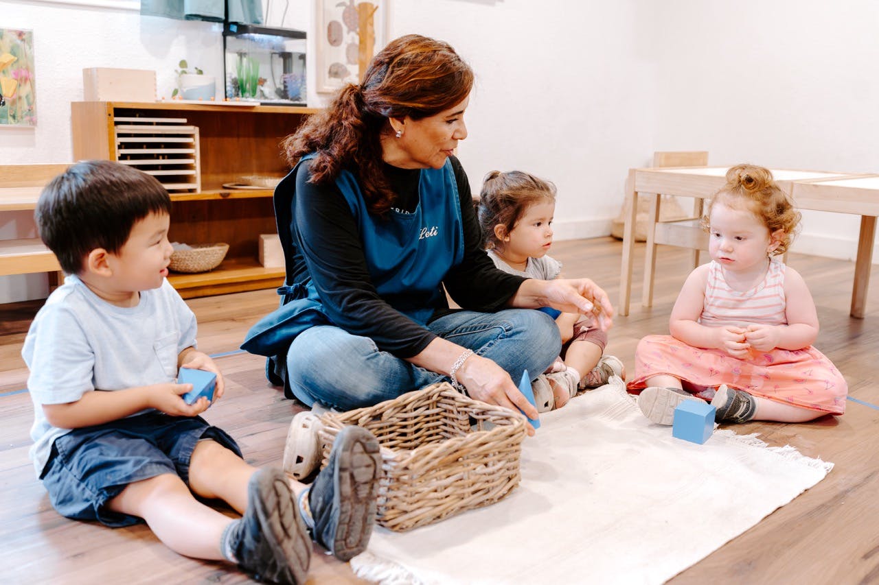 Adult and three children sitting on floor playing with blocks and basket