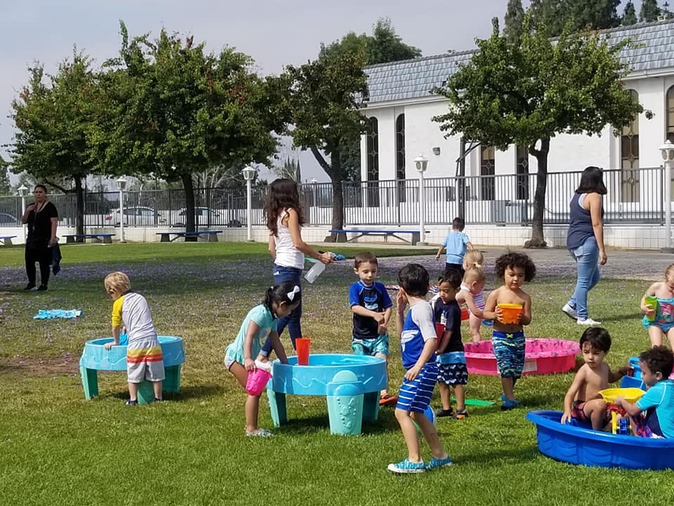 Adults and children playing with water tables and small pools on a grassy area