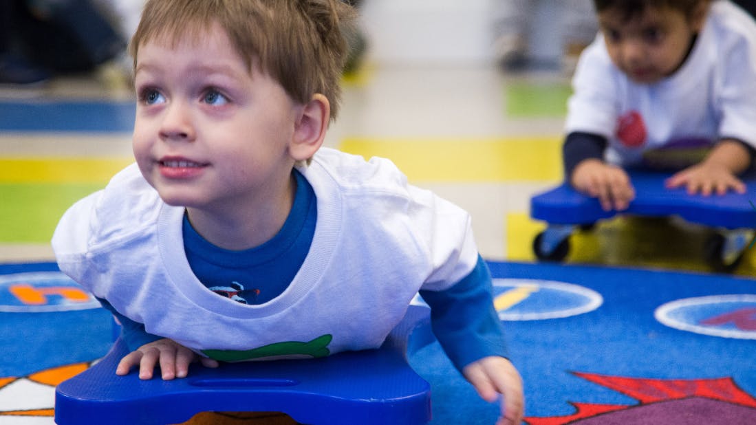Child on a blue scooter board in a classroom