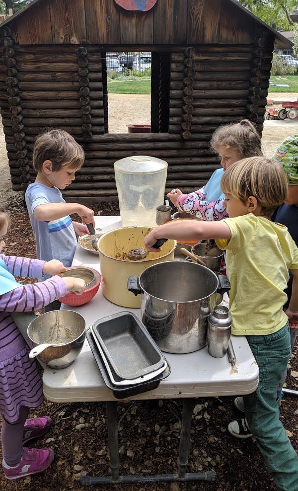 Children playing with pots and pans at a table outdoors