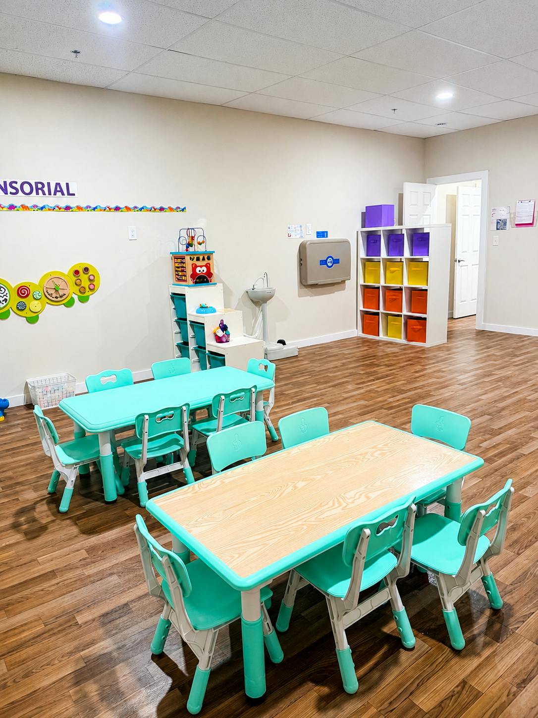Children's classroom with small tables and chairs, toys, and changing station