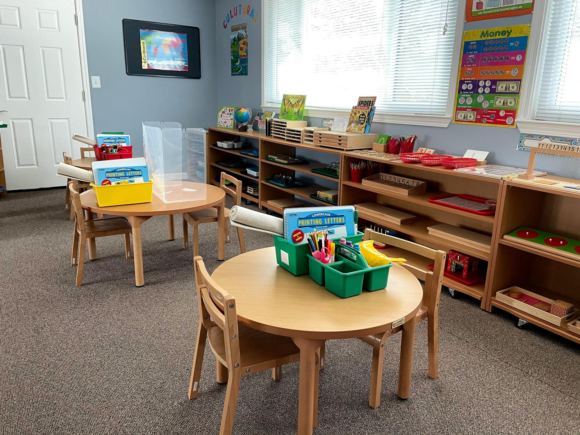 Classroom with small tables and chairs, shelves with learning materials