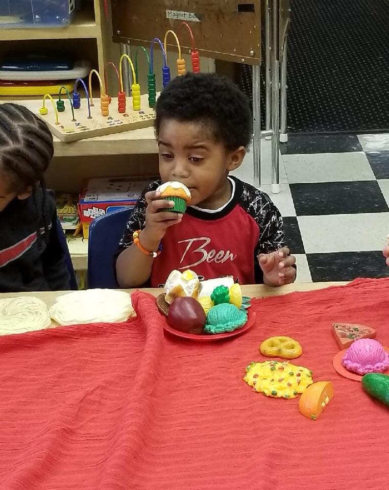 Child holding a cupcake at a table with play food