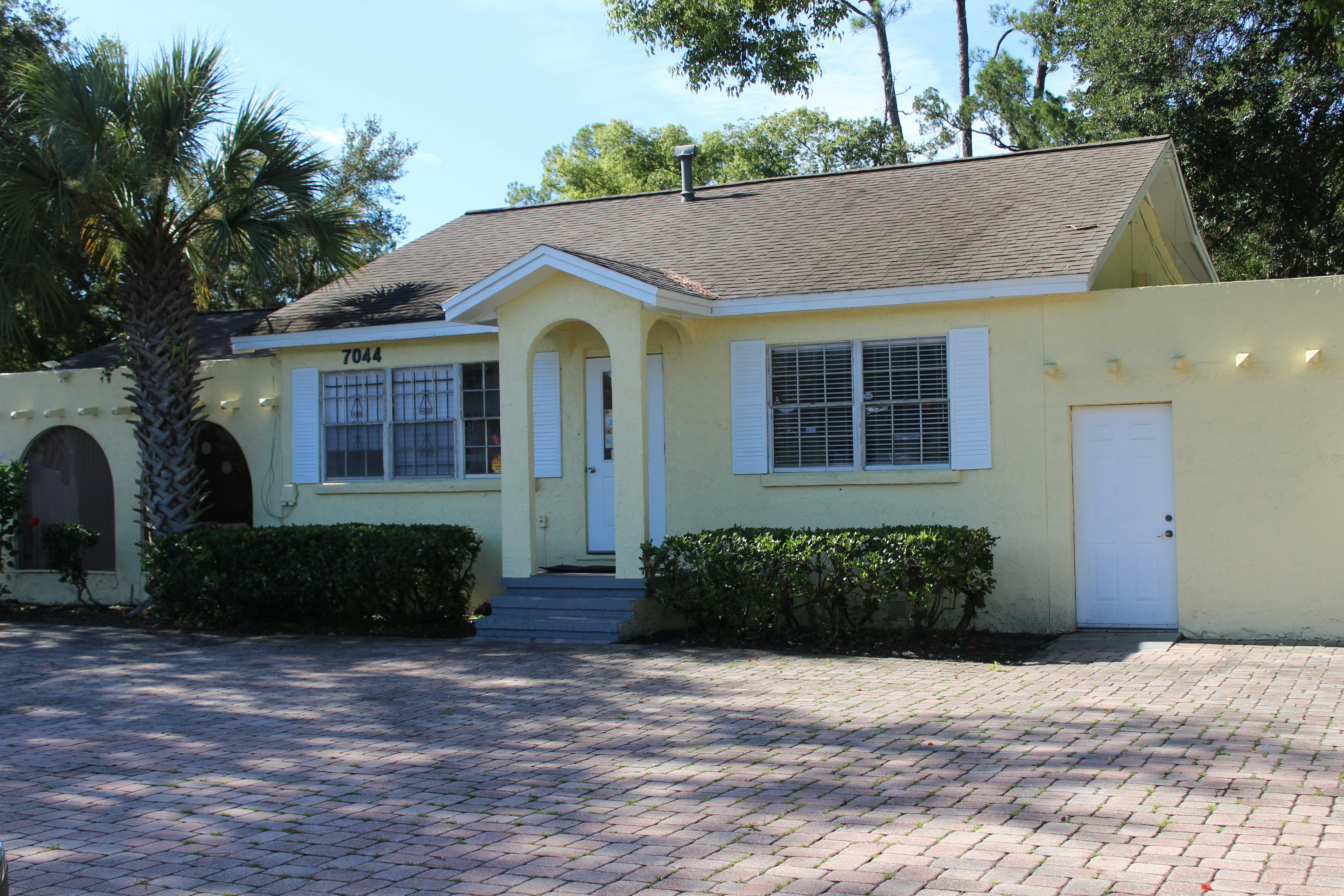 Yellow house with a palm tree and brick driveway