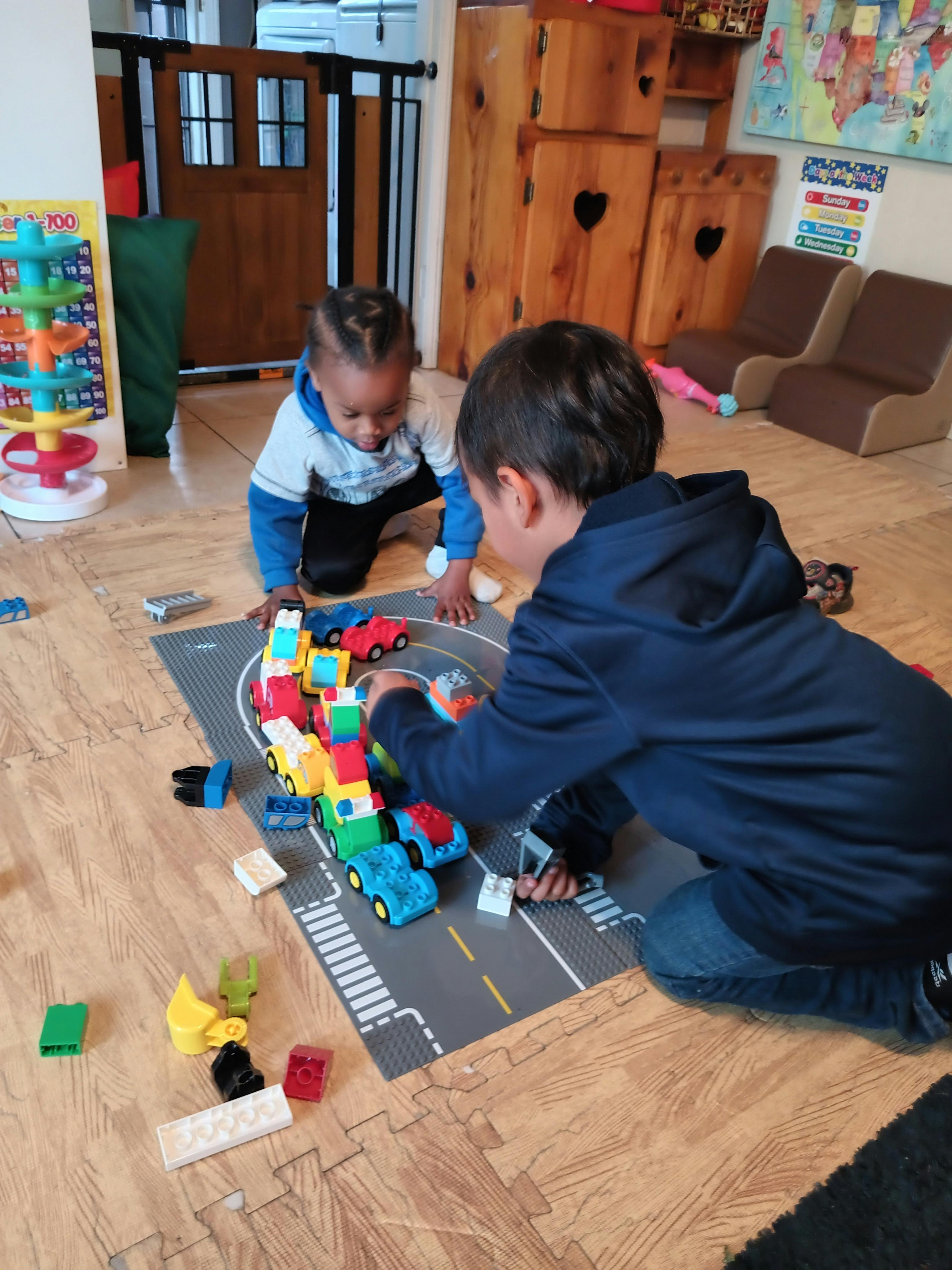 Two children playing with toy cars on a road mat