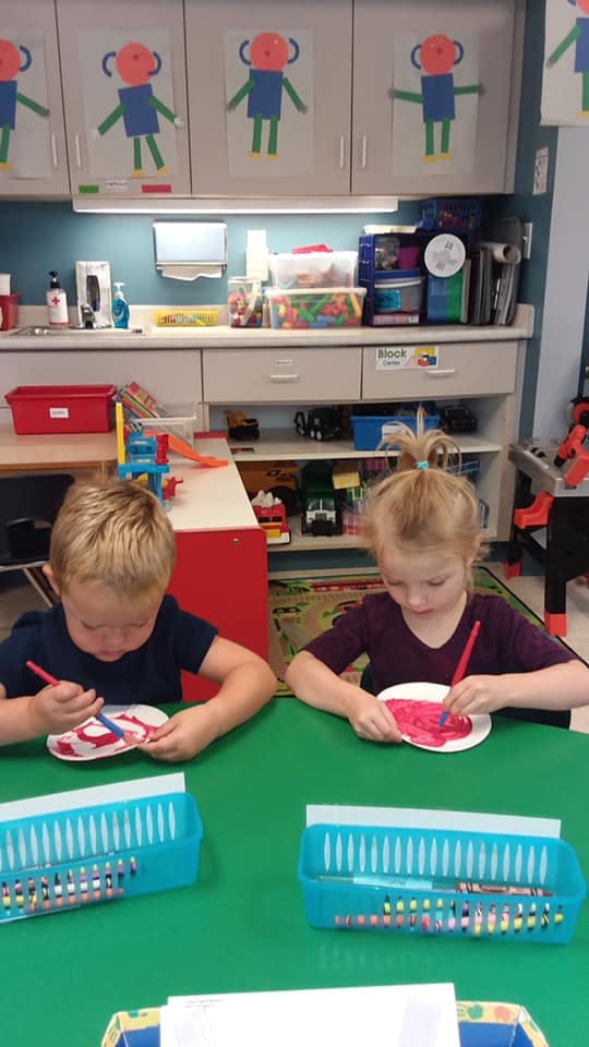 Two children painting at a table in a classroom