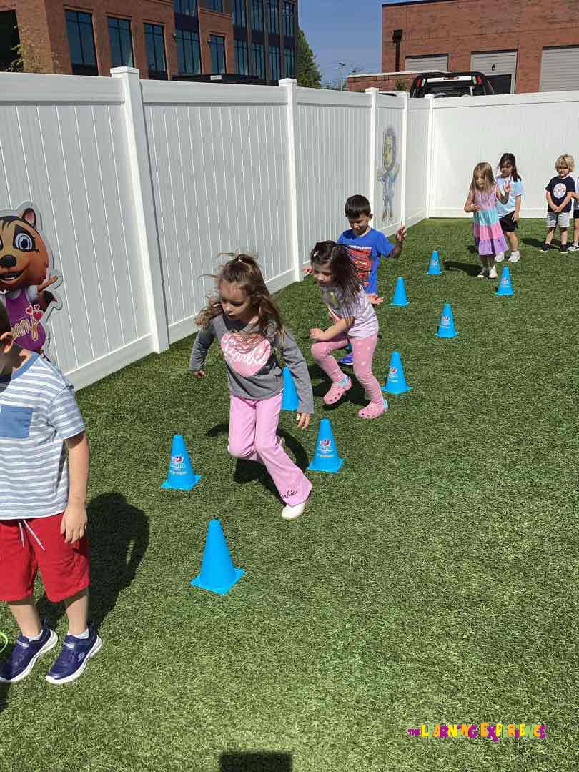 Children running through an obstacle course with blue cones on artificial grass