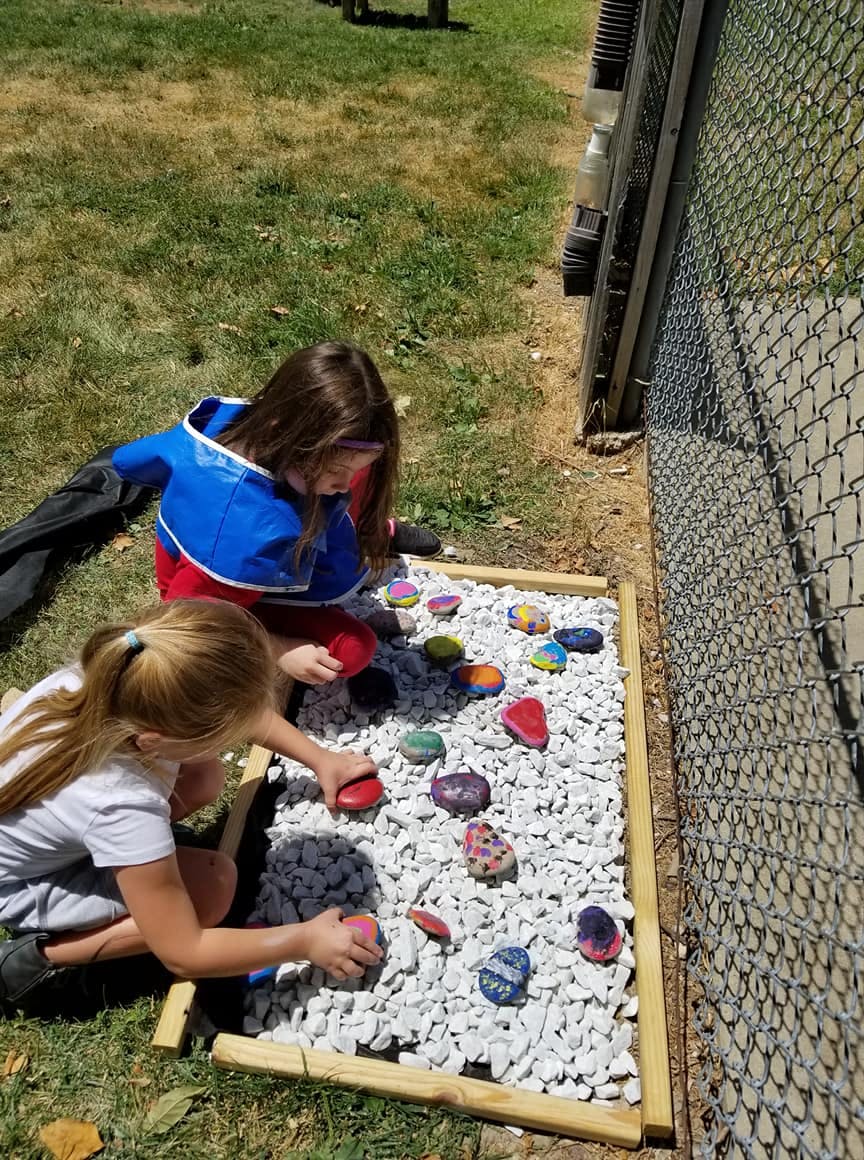 Two children placing painted rocks on white gravel