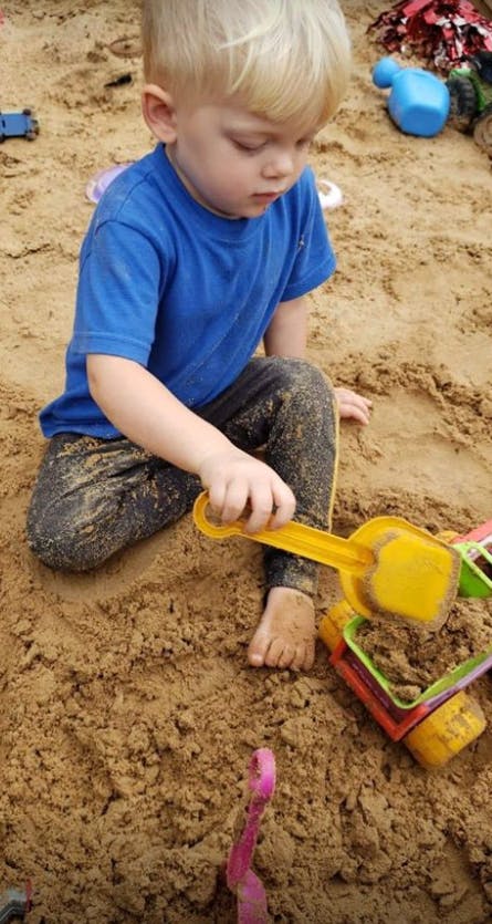 Child playing in sand with a yellow shovel