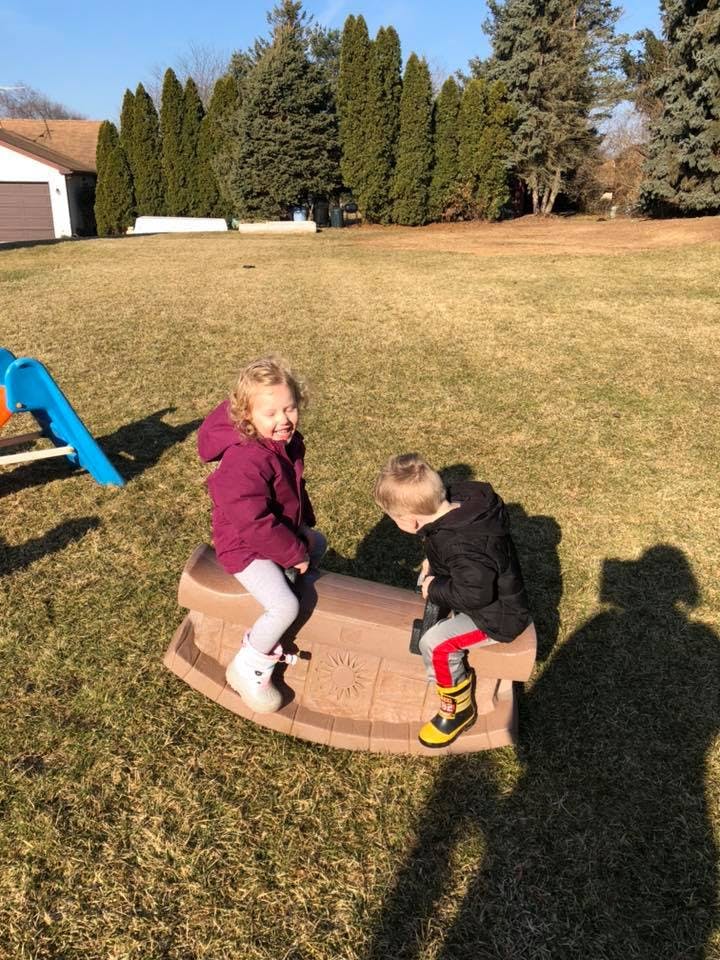 Two children on a rocking toy in a grassy yard