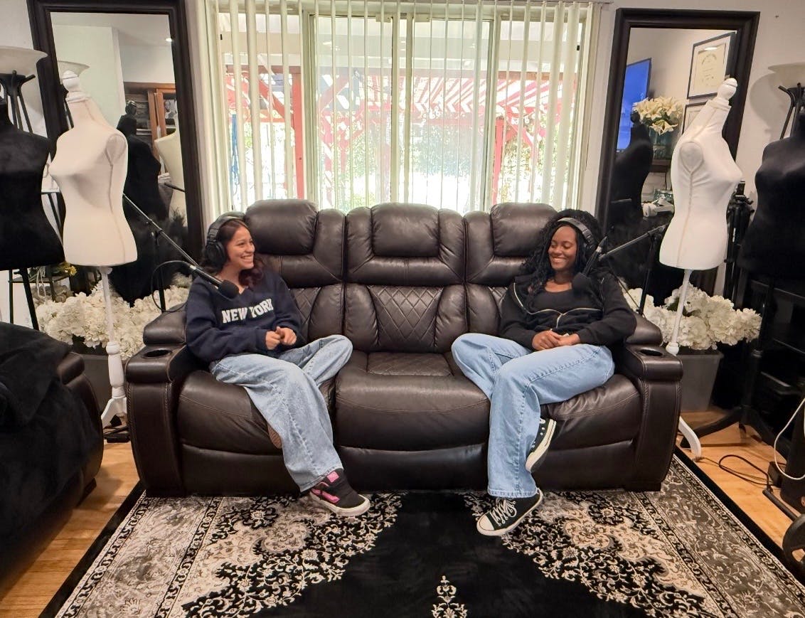 Two people wearing headphones sitting on a leather sofa with microphones