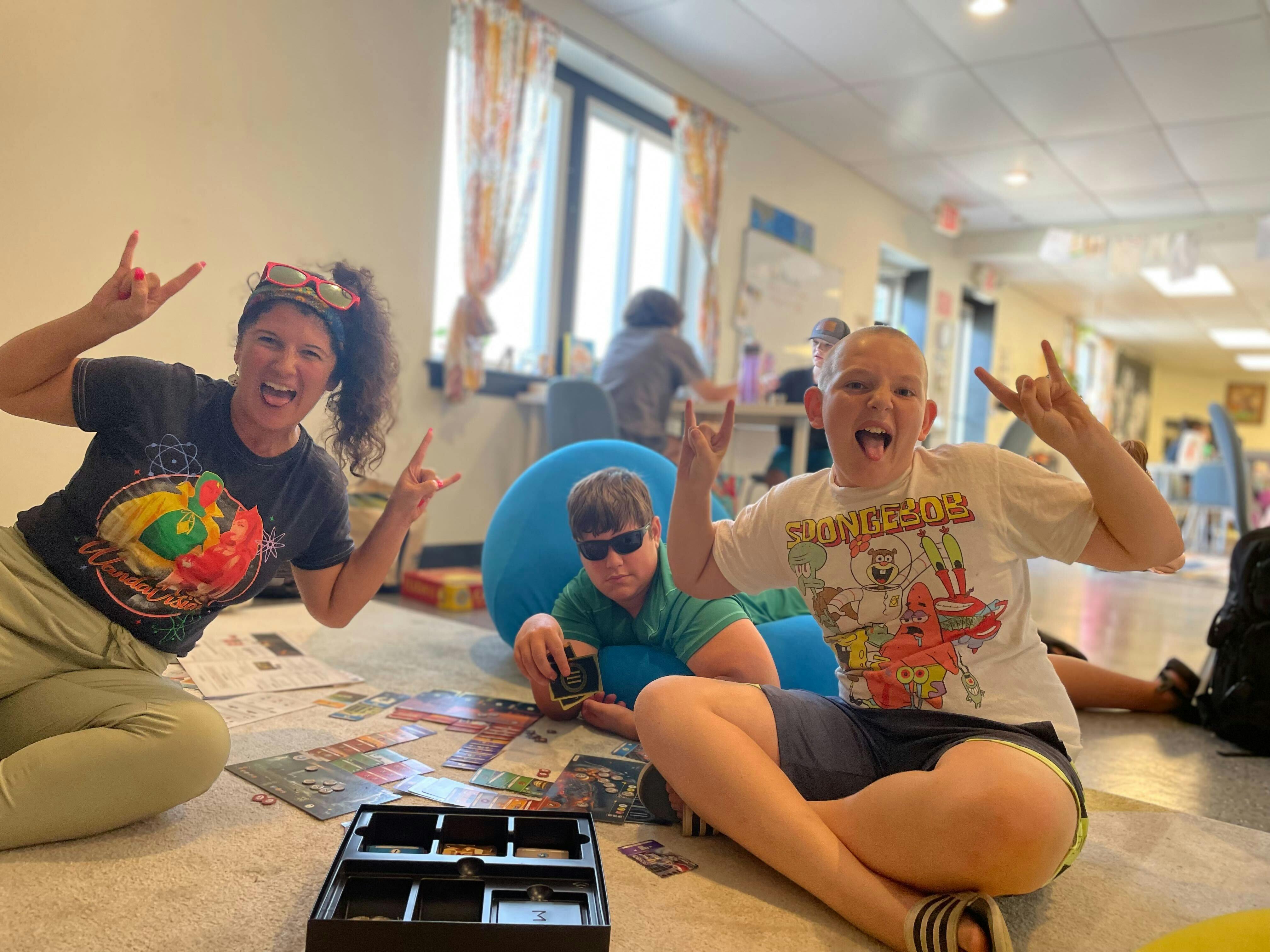 Three people making rock and roll hand gestures while sitting on the floor