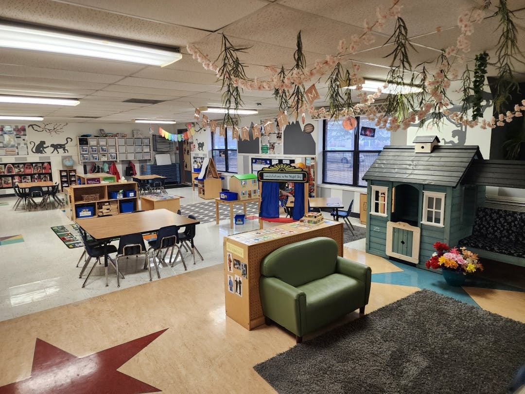 Classroom with tables, chairs, a playhouse, and an armchair