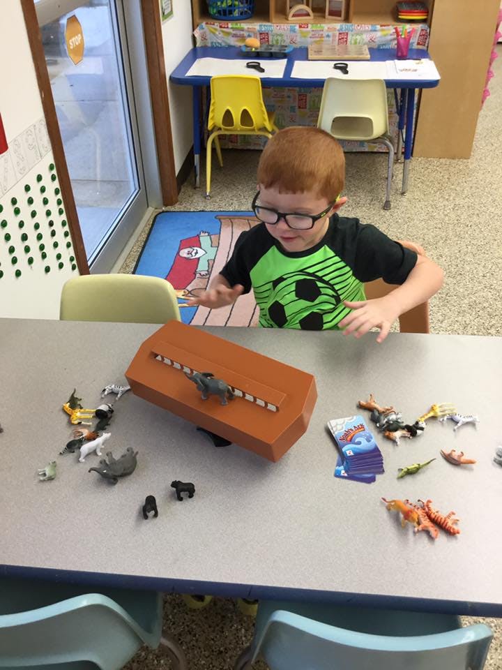 Child playing with animal figurines and a wooden toy at a table