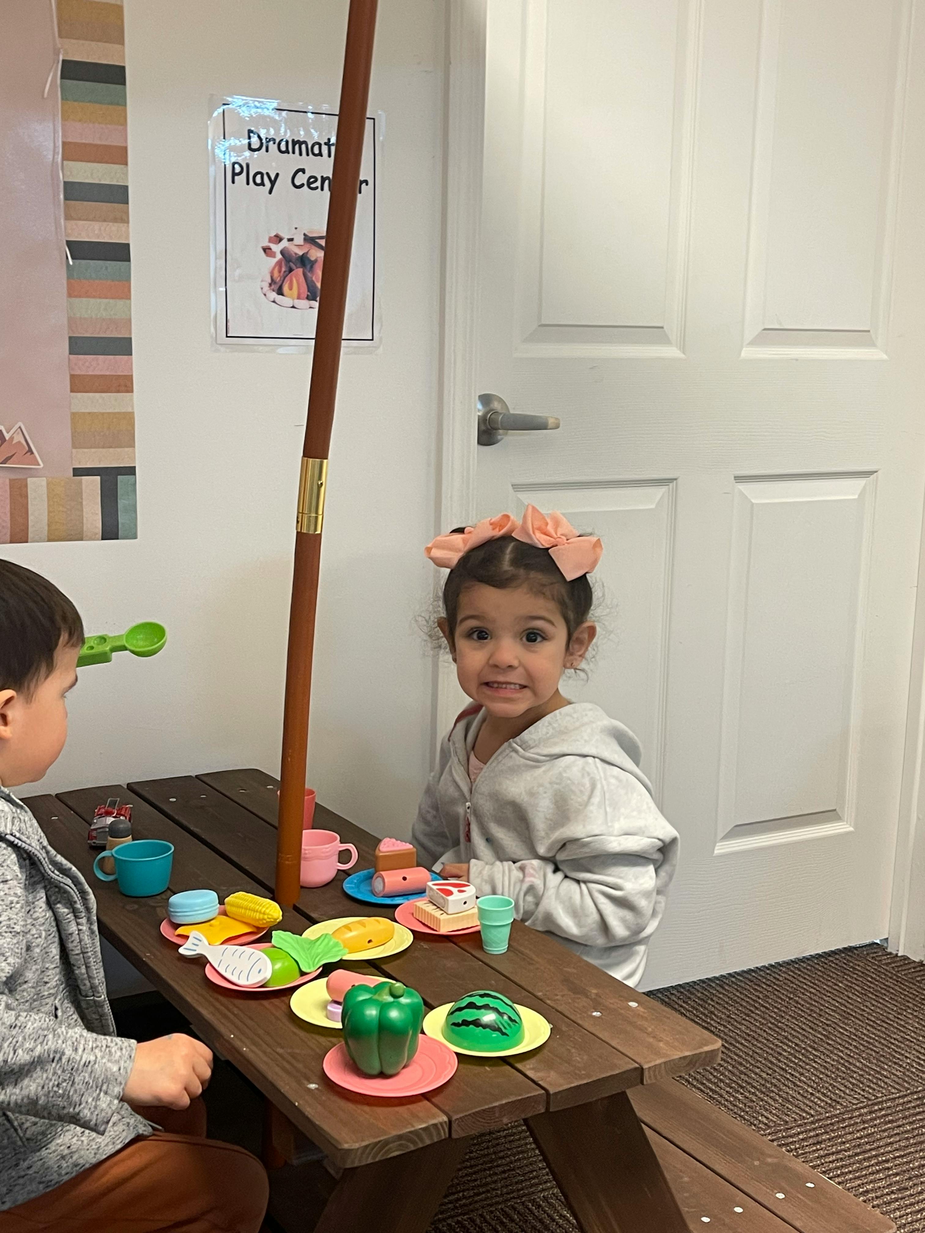 Two children playing with toy food at a small picnic table