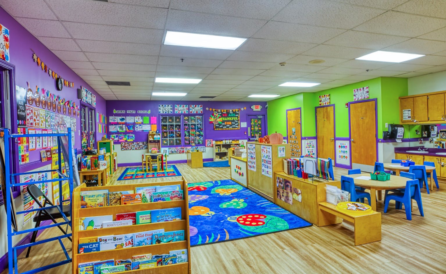 An empty, colorful classroom with tables, chairs, and shelves of books