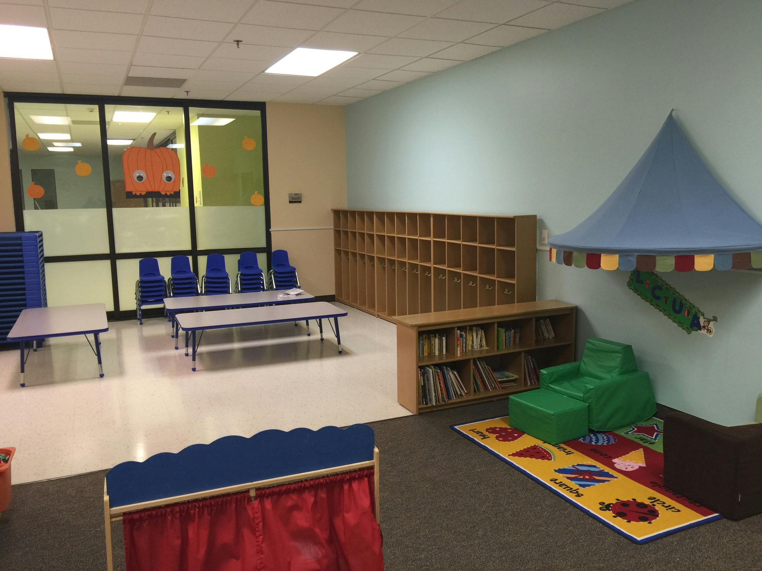 Classroom with small tables, chairs, bookshelves, and a play tent