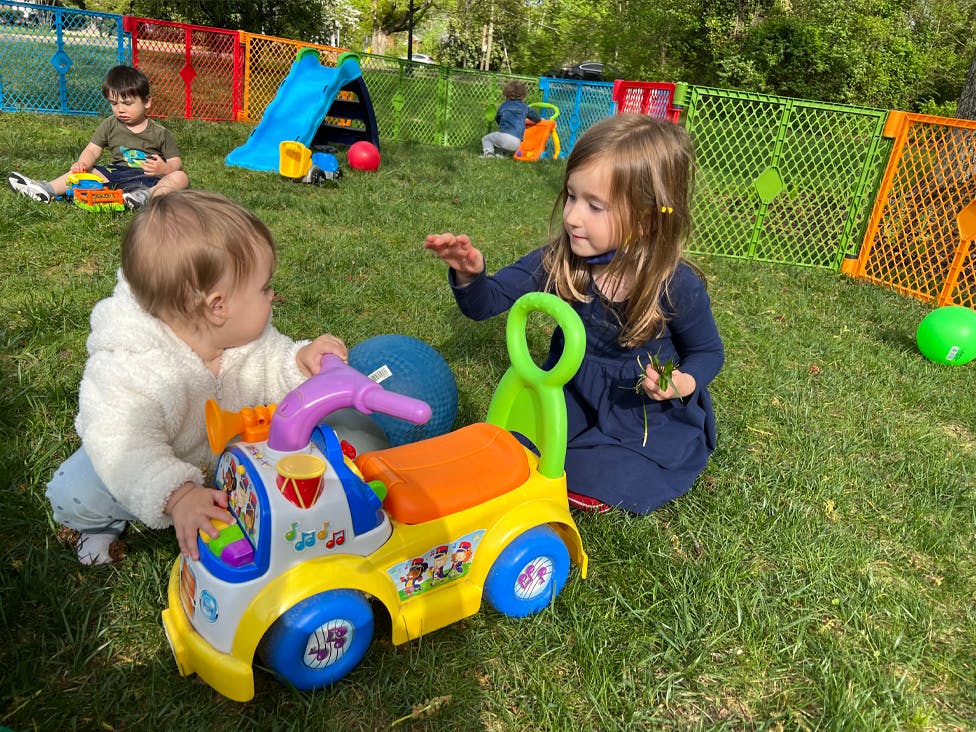 Two children playing with a ride-on toy on grass