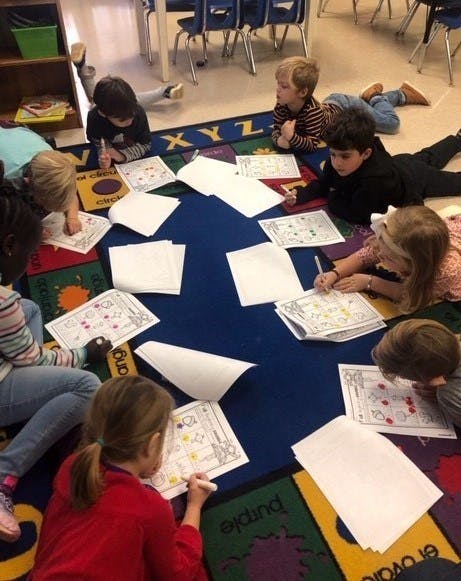 Children lying on a rug coloring worksheets in a classroom