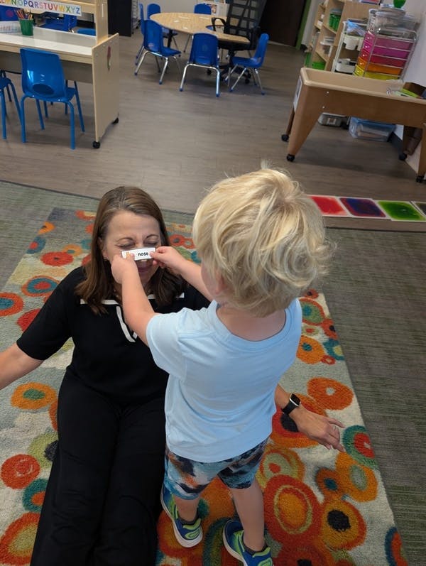 A child placing a card labeled nose on a person's face in a classroom