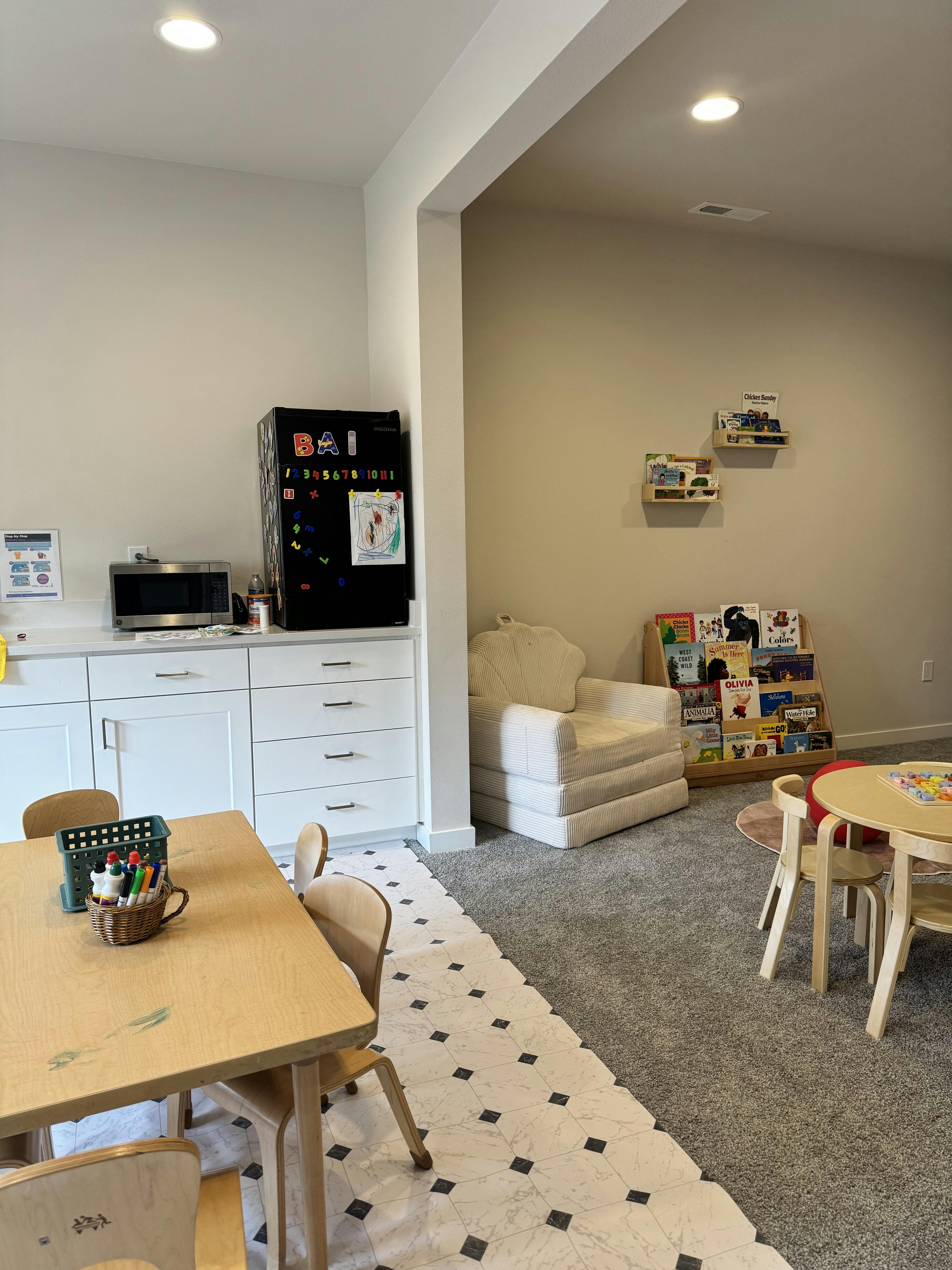A children's playroom with small tables, chairs, bookshelves, and an armchair