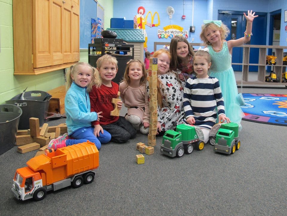 Group of children playing with toy trucks and blocks in a classroom