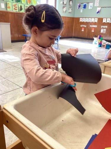 Child cutting black paper with scissors in a classroom