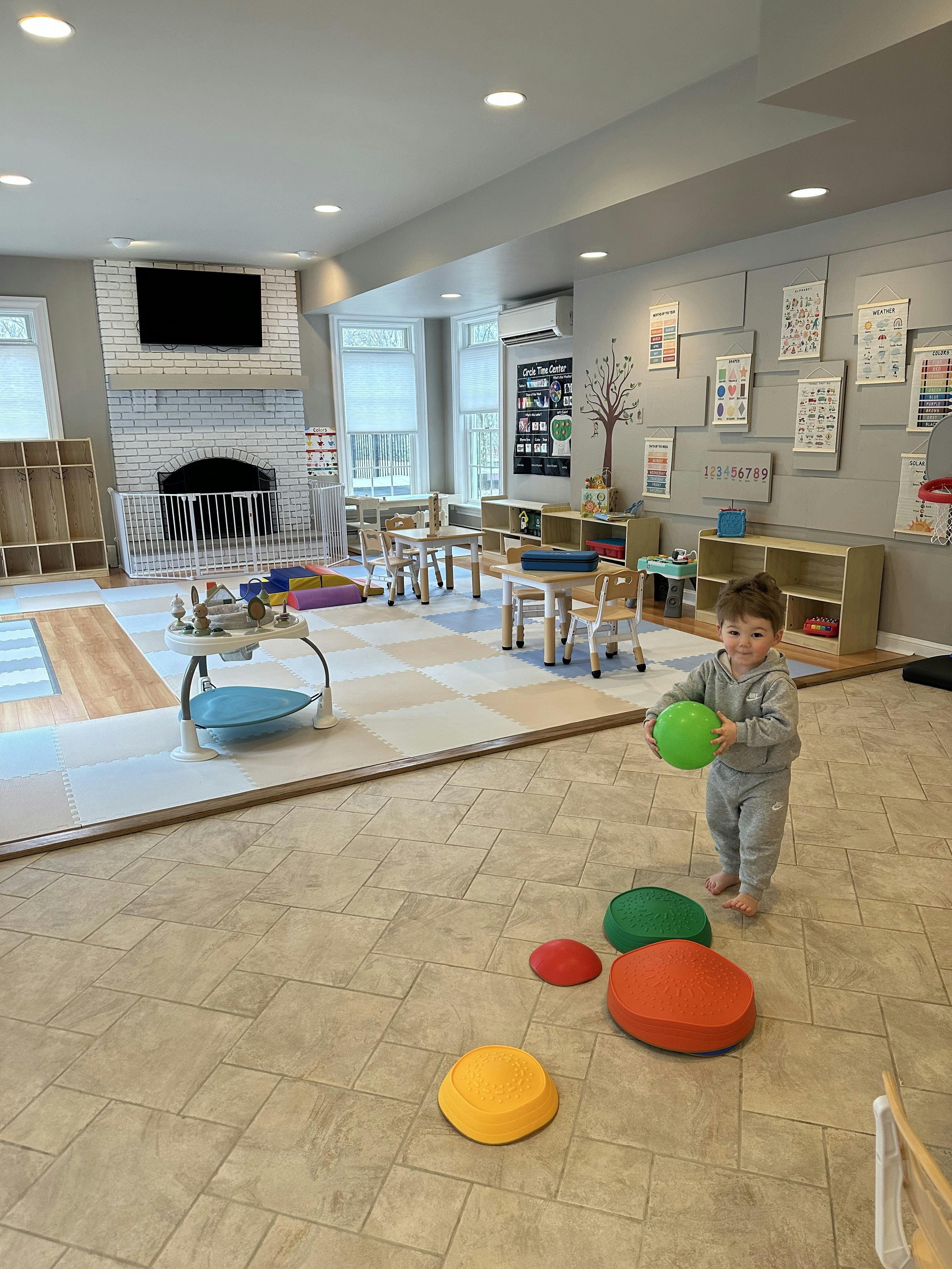 Child in a playroom holding a green ball