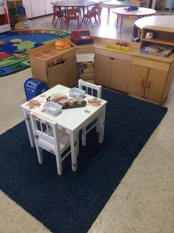 Playroom with child-sized table and chairs on a rug, play kitchen, and other furniture