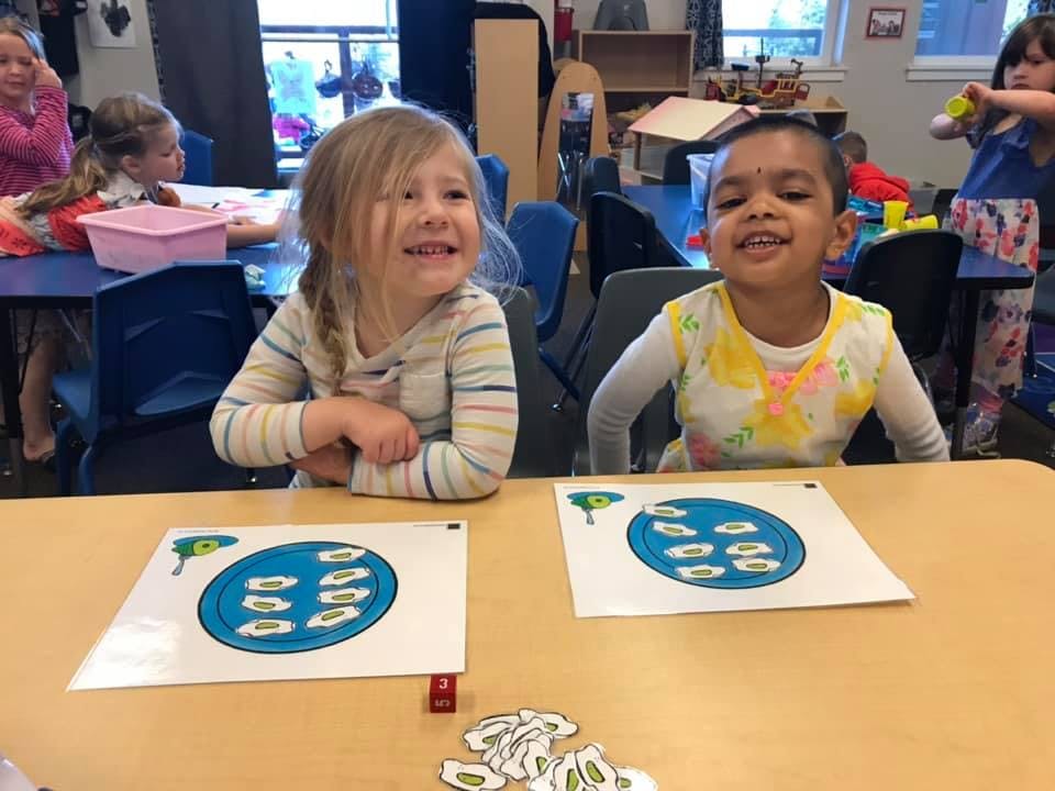Two children at a table with learning materials in a classroom