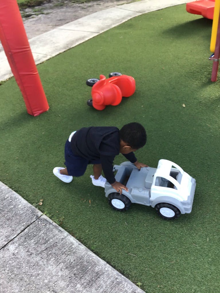 Child on hands and knees playing with a toy truck on artificial grass