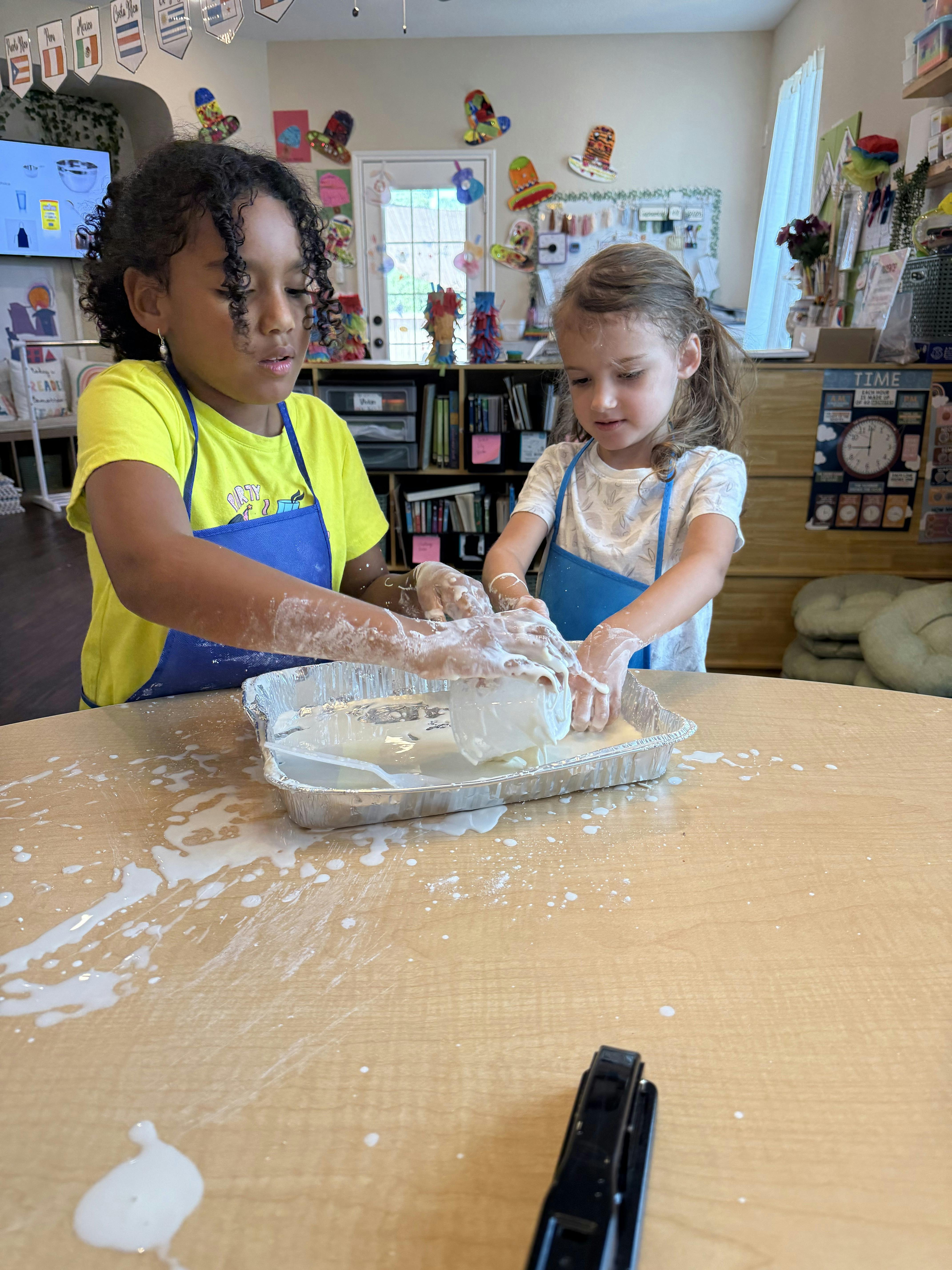 Two children wearing aprons playing with white goop in a pan