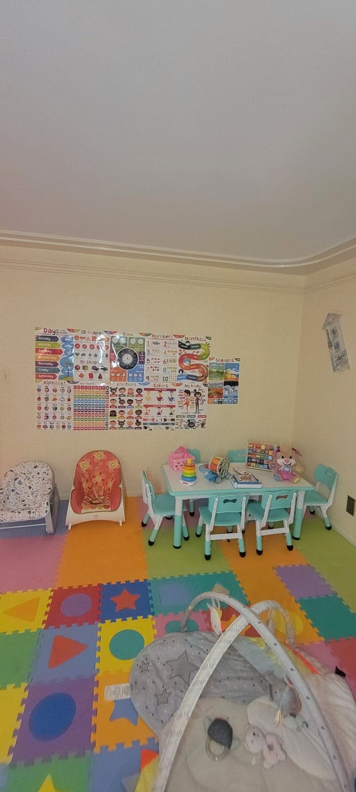 A classroom with colorful floor mats, a small table with chairs, and posters on the wall