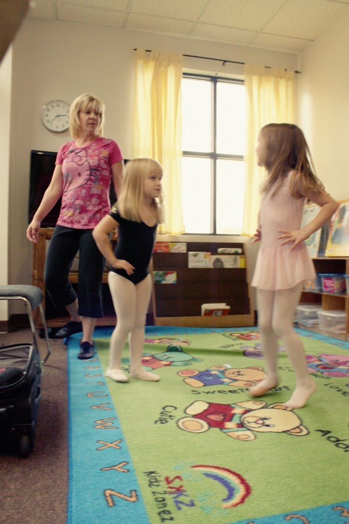 Adult and two children in dance attire standing on a colorful rug