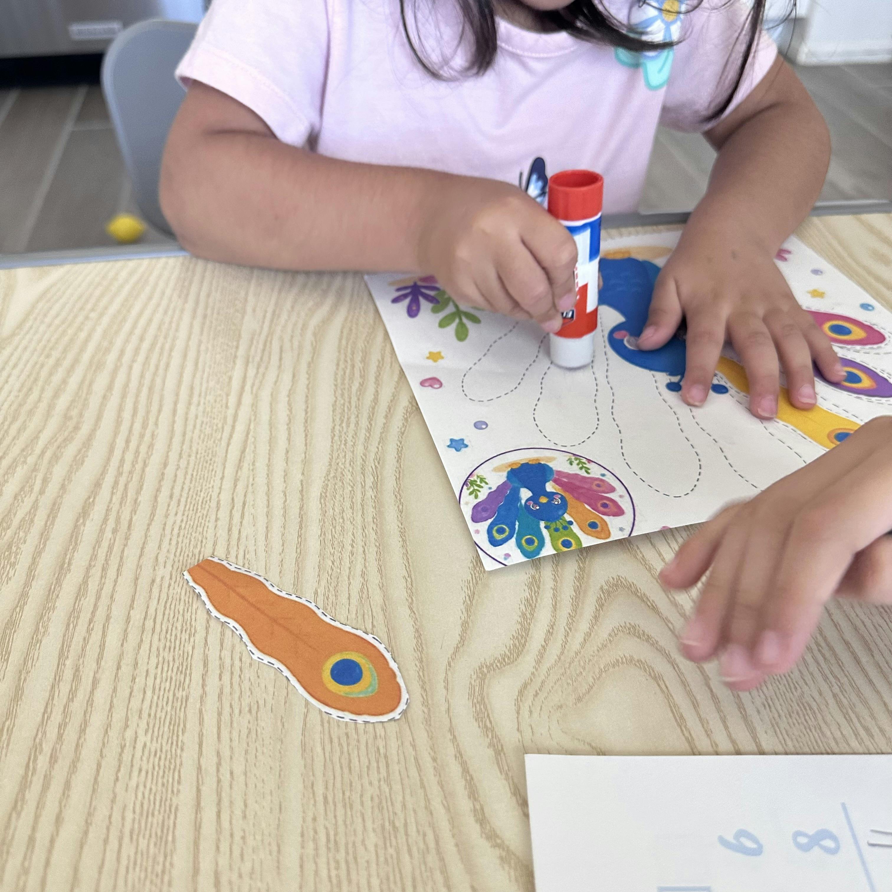 Child using a glue stick on a paper craft of a peacock