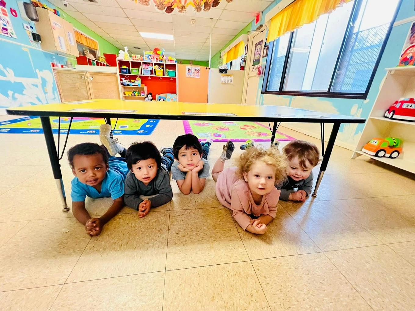 Four children lying on the floor under a table