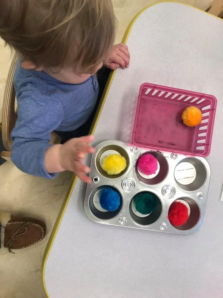 Child playing with colorful pom-poms in a muffin tin