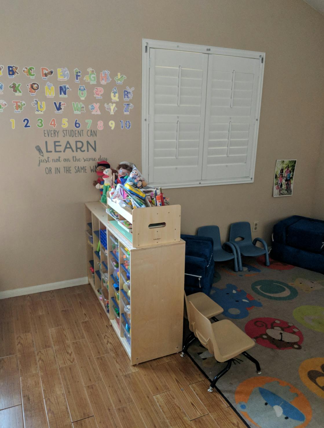 Classroom with alphabet and numbers on wall, storage unit, small chairs, and rug