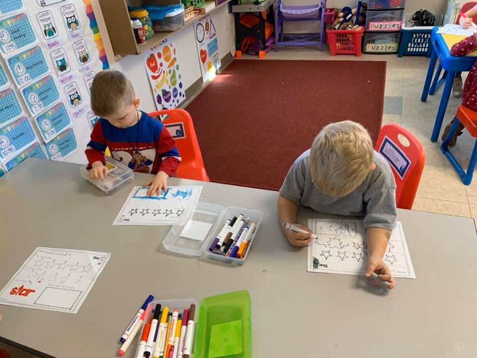 Two children drawing at a table in a classroom