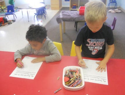 Two children drawing at a red table in a classroom