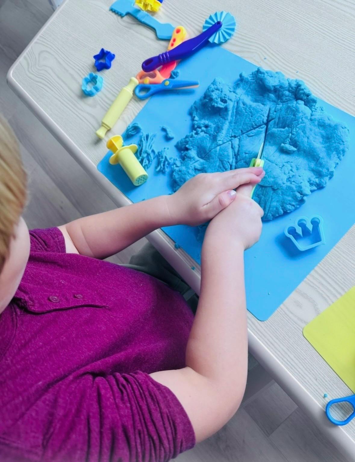 Child playing with blue modeling clay and plastic tools
