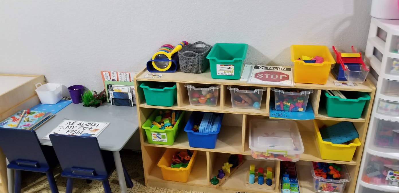 Classroom with a table and chairs next to a wooden shelf with colorful bins
