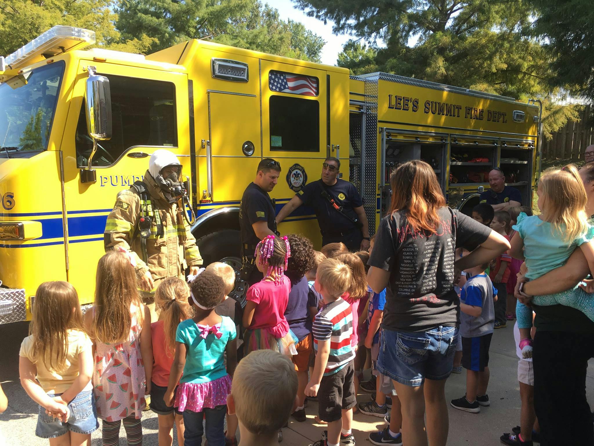 Firefighter in gear with children and adults in front of a fire truck