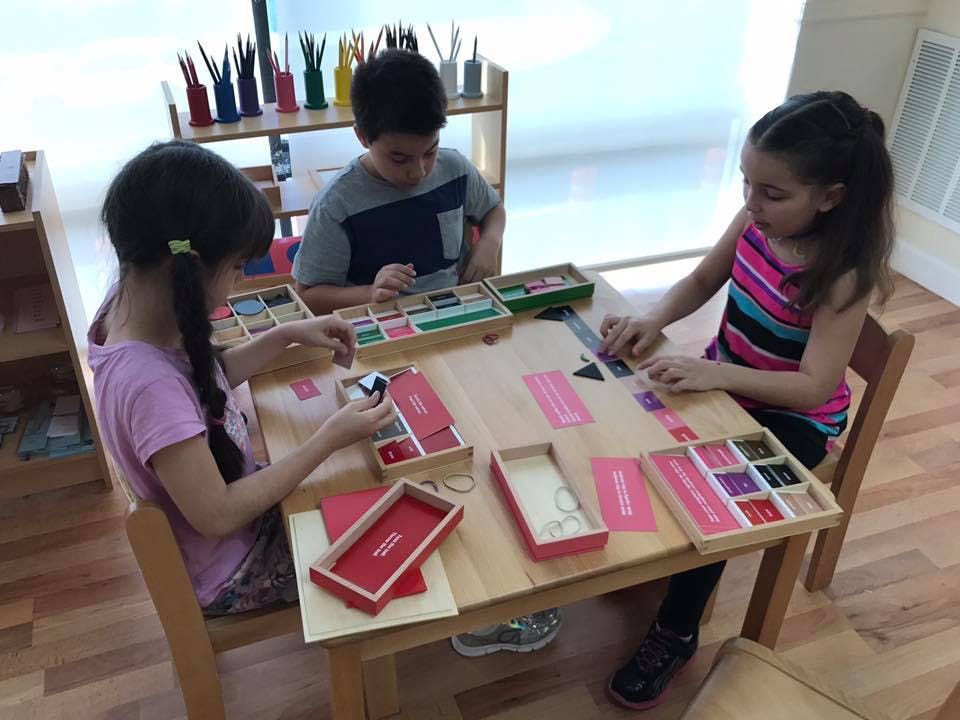 Three children at a table playing with educational materials